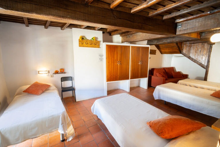 Habitación de 4 plazas abuhardillada con camas individuales, sofá y techo de madera en Albergue Rural San Blas