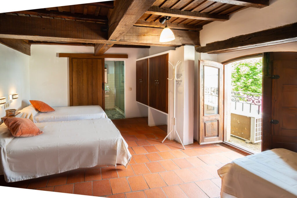 Habitación de 4 plazas con balconera exterior, camas individuales y suelo de barro en Albergue Rural San Blas